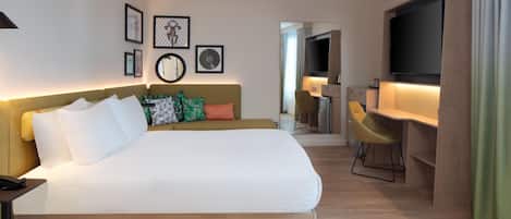 Ett hotellrum med en stor säng, ett skrivbord, en stol, en tv och en spegel.