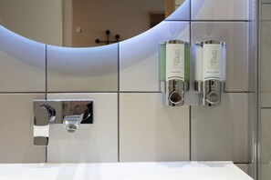 A bathroom with a modern design, featuring a large mirror, a chrome faucet, and two hand soap dispensers labeled 'Therapy Water Therapy'. - Hampton by Hilton York Piccadilly (York)