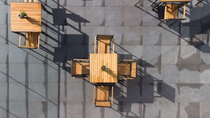 A top-down view of a patio area with wooden tables and chairs, arranged in a square pattern.