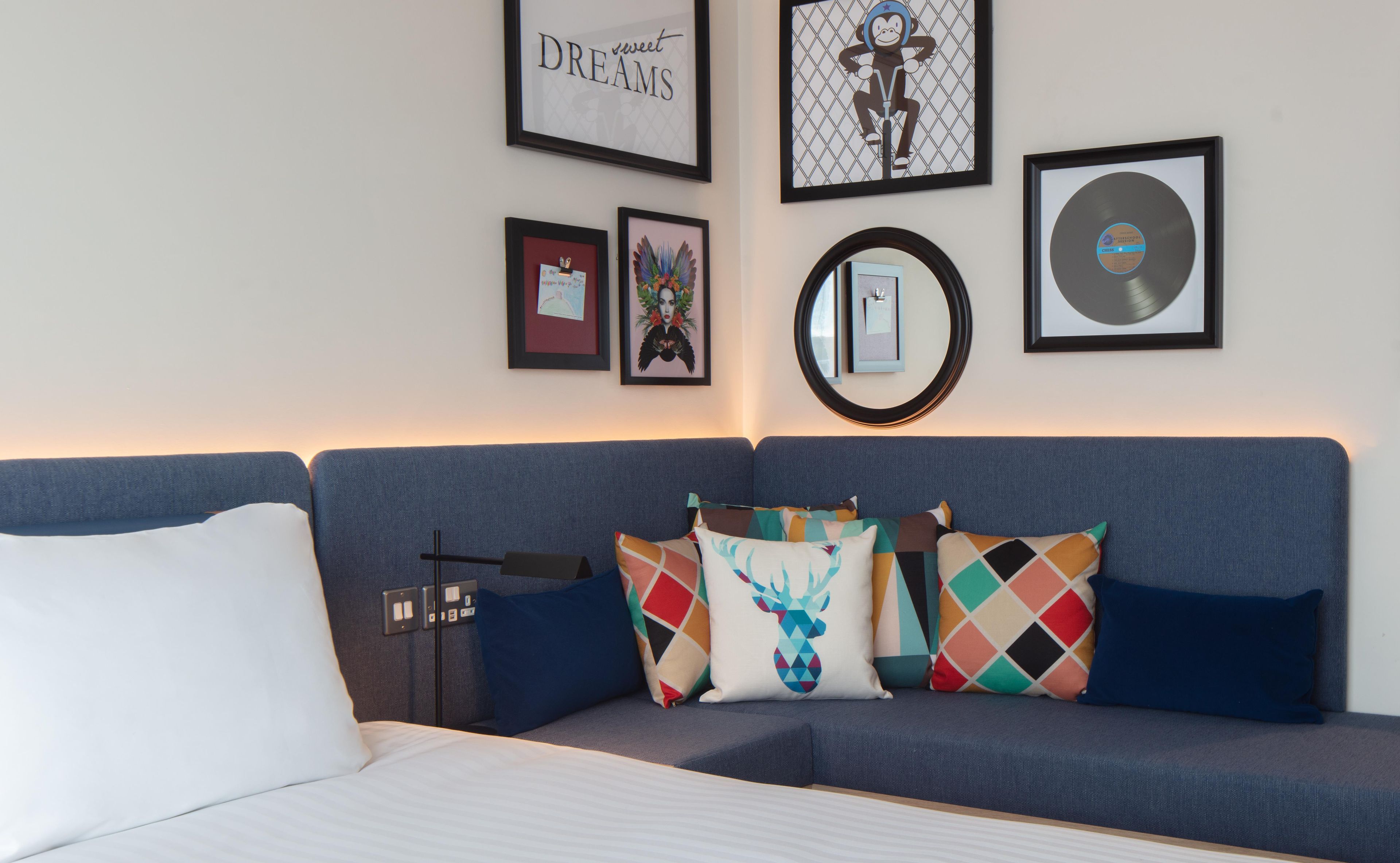 Een kamer met een blauwe bank, kleurrijke kussens en kunstwerken in lijsten aan de muur.