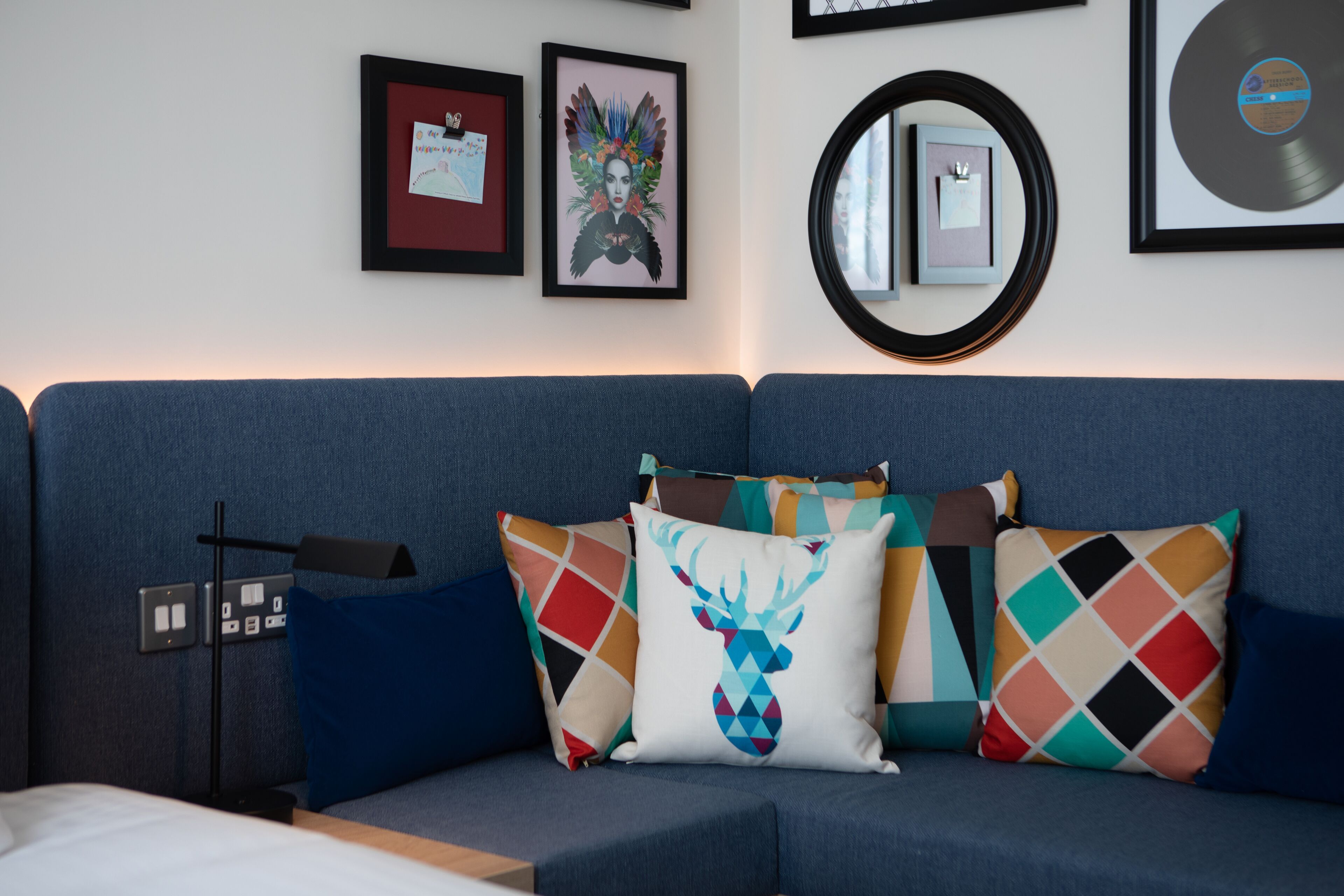A modern living room with a blue sofa, colorful patterned cushions, framed artwork, and a record on the wall.