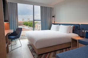 Habitación de hotel con una cama grande, un escritorio, una silla y vistas a la ciudad.