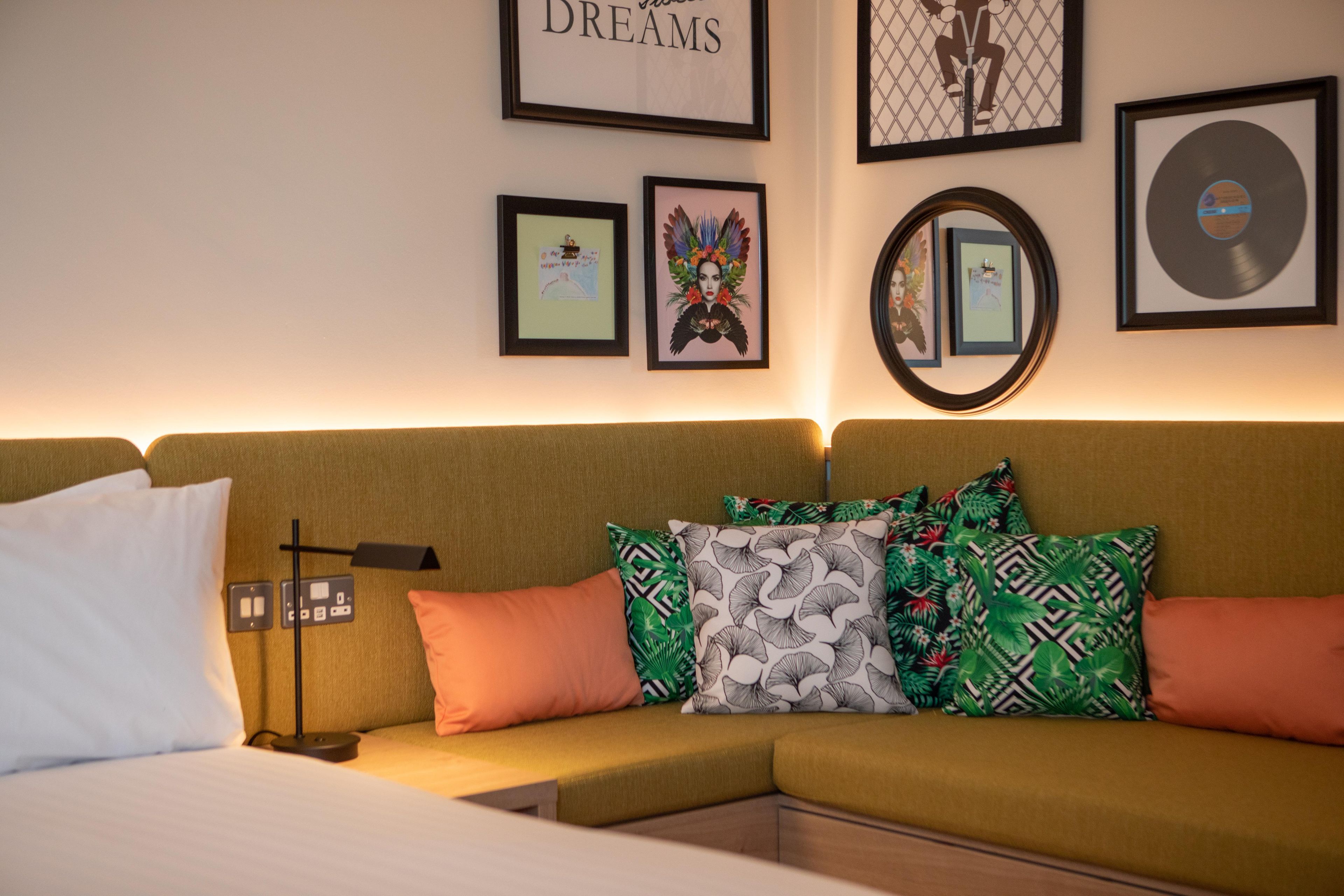Una habitación con un sofá verde, varios cojines, una lámpara de pared y cuadros enmarcados.