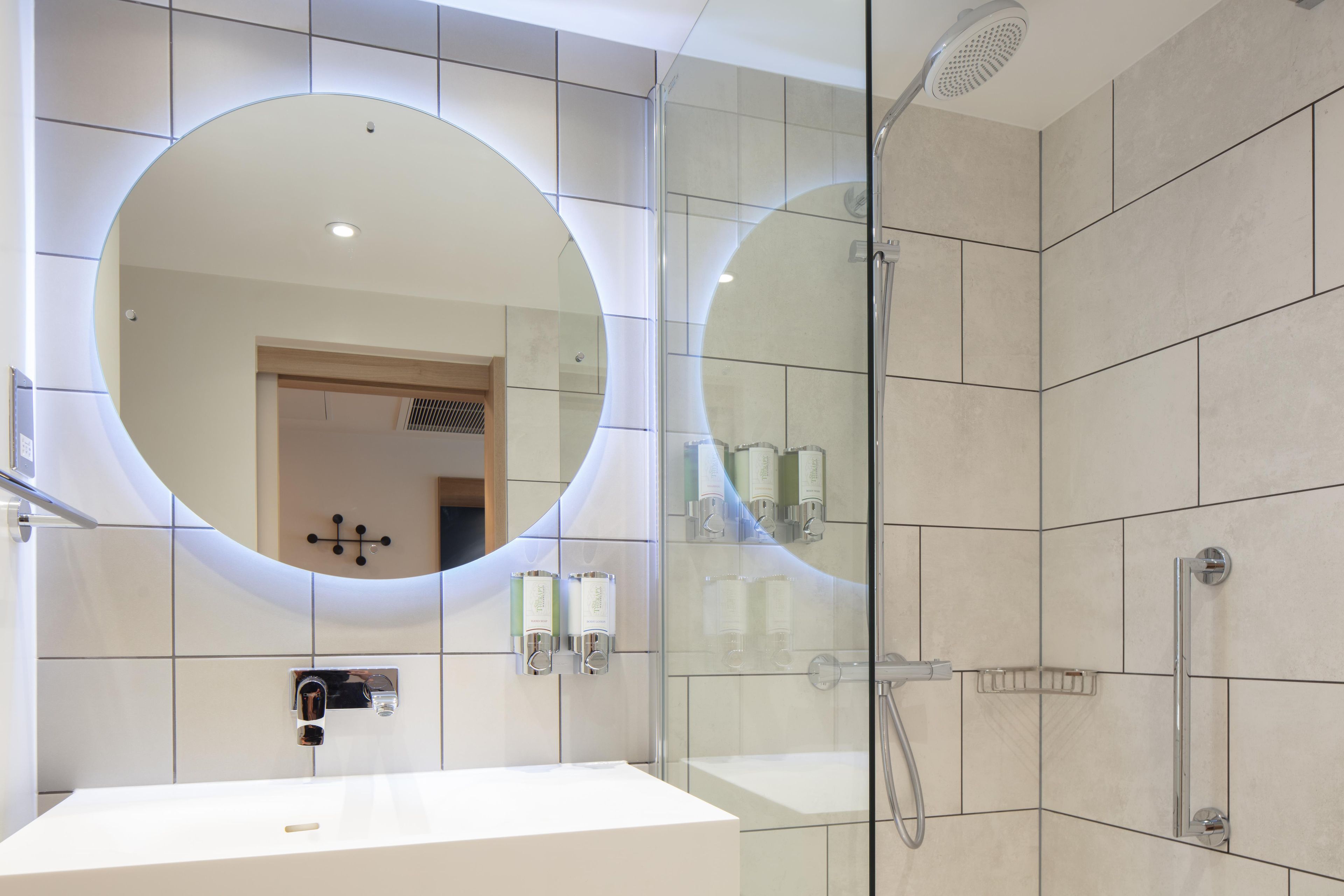 Un baño moderno con un espejo grande, una ducha y un lavabo.
