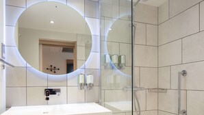 A modern bathroom with a large mirror, a shower, and a sink.