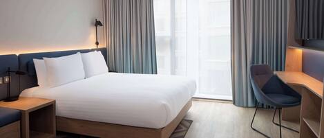 A modern hotel room with a large bed, a desk, and a chair.