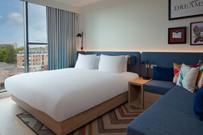 A modern hotel room with a large bed, a sofa, and a view of the city. - Hampton by Hilton York Piccadilly (York)