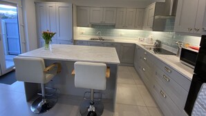 Una cocina moderna con armarios grises, encimera de mármol y electrodomésticos de acero inoxidable. Hay dos taburetes de bar y un jarrón con flores en la encimera.