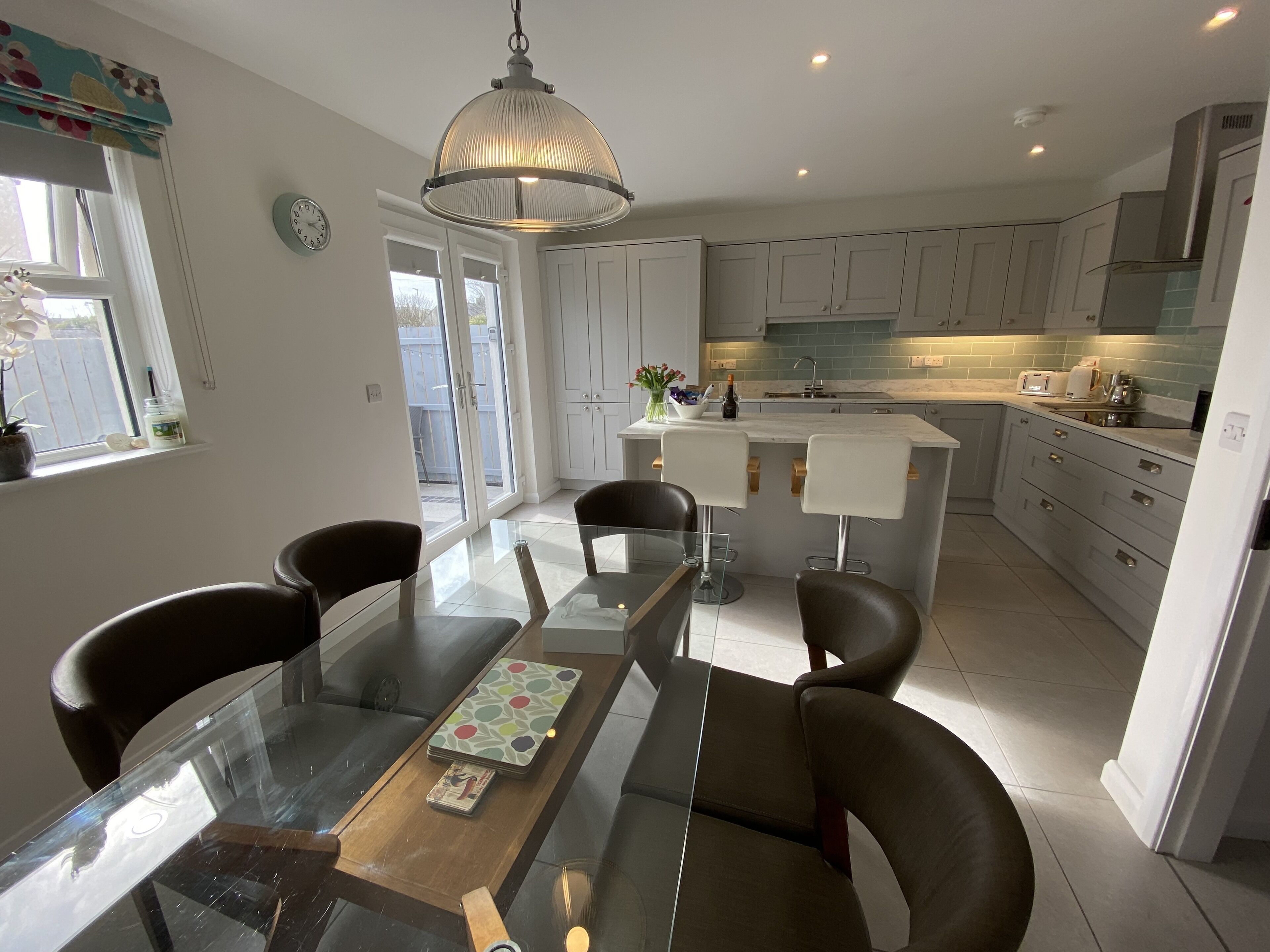 A modern kitchen with white cabinets, a central island with bar stools, and a dining table with chairs.