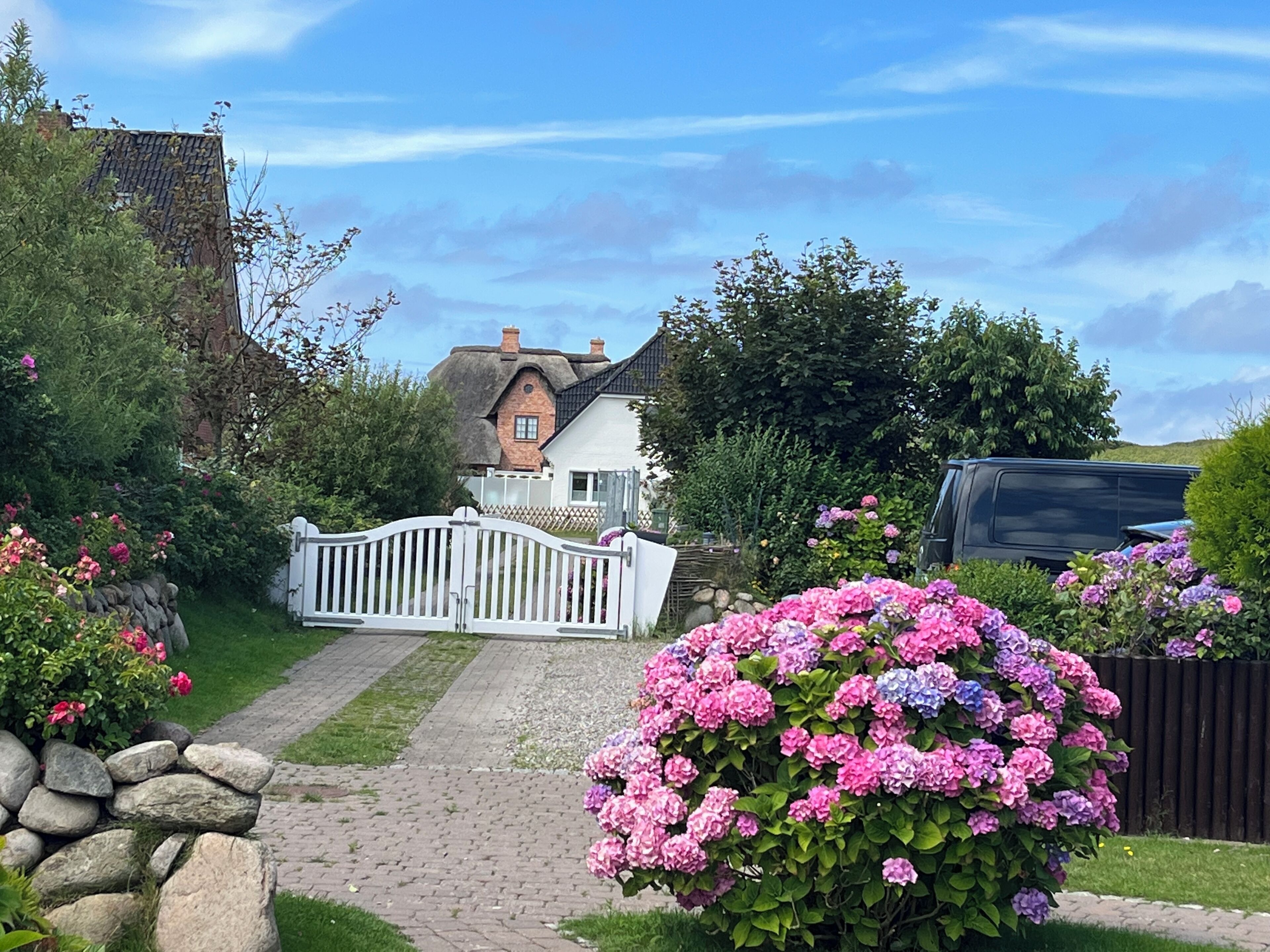 A quaint house with a white picket fence, a stone pathway, and vibrant pink and purple flowers.