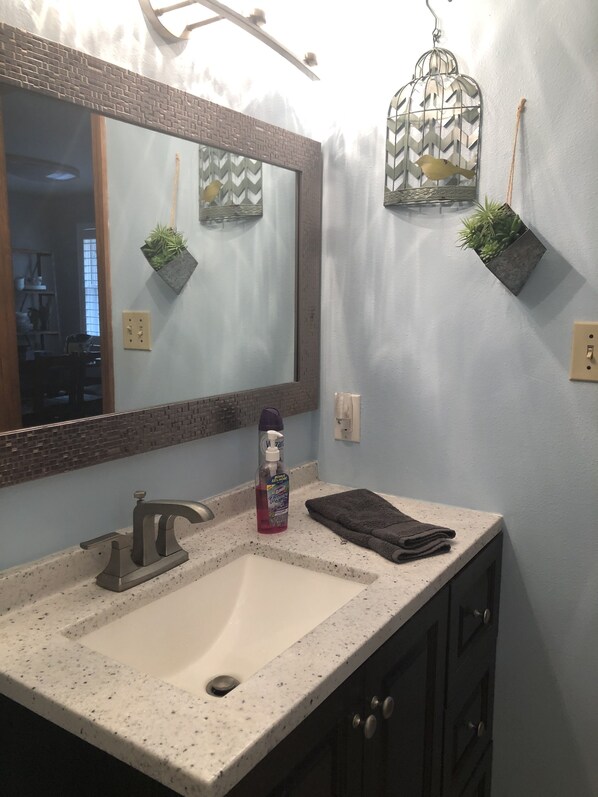 A bathroom with a large mirror, a sink, a towel, and decorative items including a birdcage and a plant.