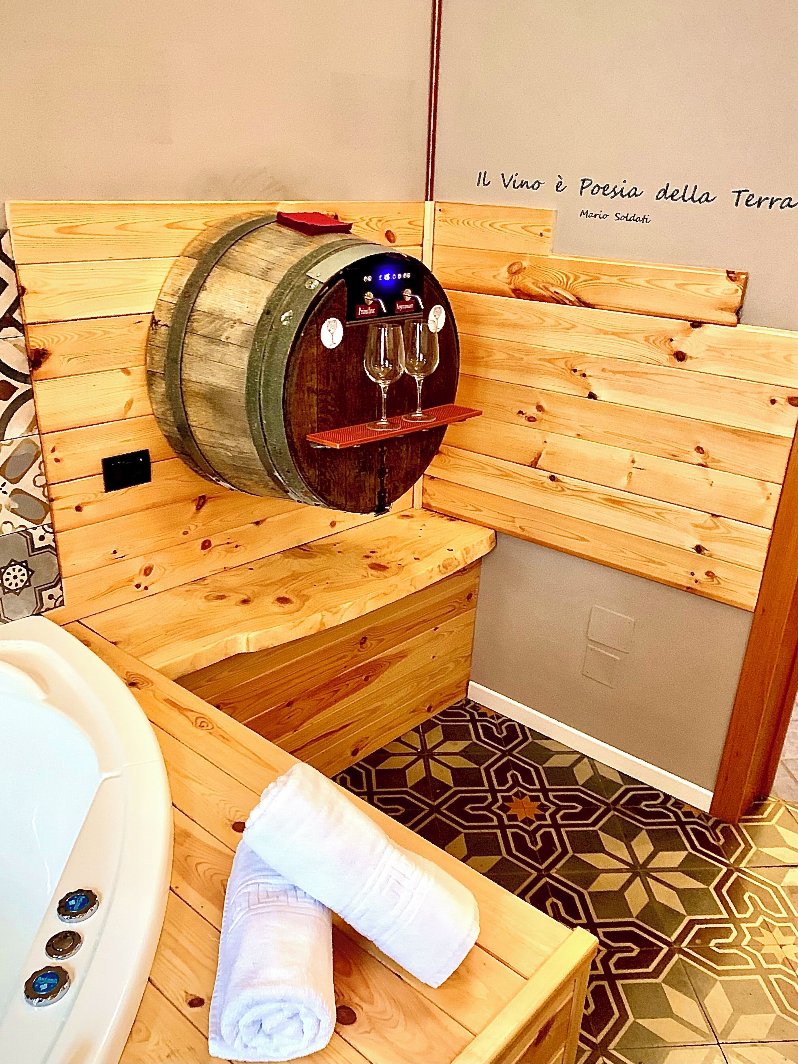 Une salle de spa en bois équipée d’un distributeur de vin, d’une baignoire et d’une serviette posée sur un banc en bois.