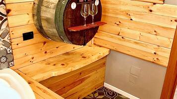 Une salle de spa en bois équipée d’un distributeur de vin, d’une baignoire et d’une serviette posée sur un banc en bois.