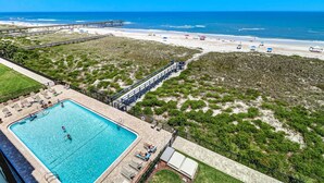 Un espace piscine offrant une vue sur la plage et l’océan, entouré de verdure et doté d’une terrasse en bois.