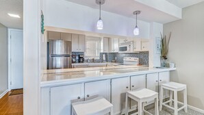 Une cuisine moderne avec des meubles blancs, un réfrigérateur en acier inoxydable, un évier à deux bacs et des luminaires suspendus.
