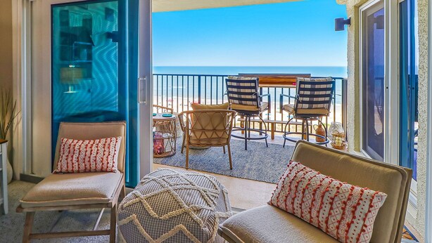Un balcon avec vue sur l’océan, aménagé avec deux chaises et un canapé, et une porte vitrée donnant sur une pièce.