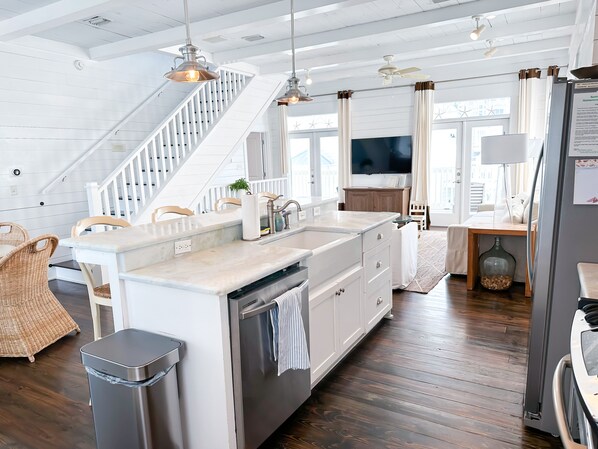 Una cocina moderna con una isla central, armarios blancos, electrodomésticos de acero inoxidable y una escalera que sube a otro nivel.
