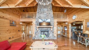Un chalet spacieux doté d’une cheminée en pierre, de planchers en bois et d’un canapé rouge.