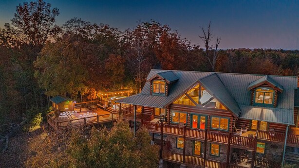 Une cabane en rondins à plusieurs étages, dotée d’une terrasse et d’un espace salon extérieur, le tout entouré de forêt.