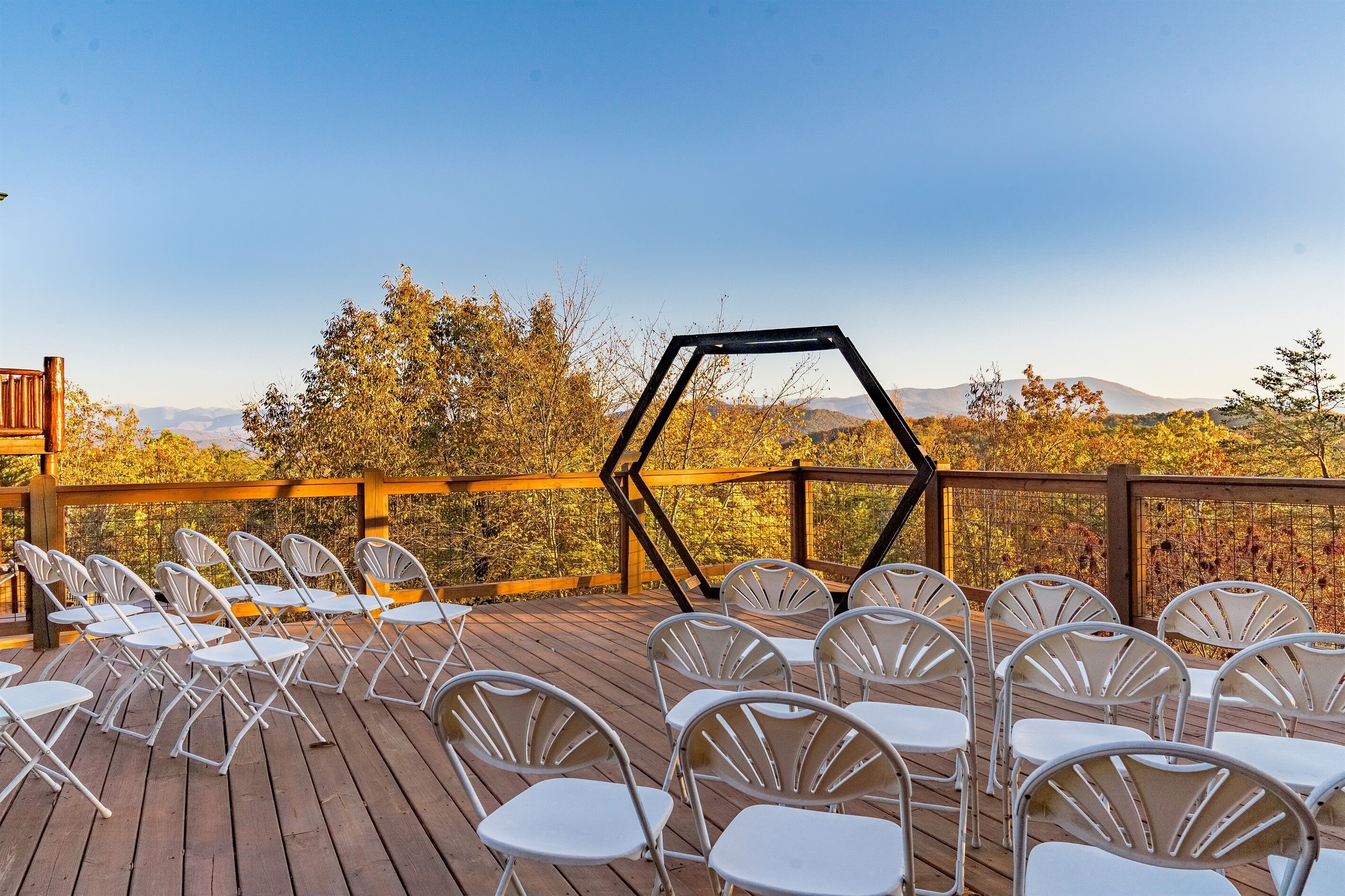 Une terrasse en bois, agrémentée de chaises blanches disposées pour un événement, et offrant une vue sur un paysage montagneux.