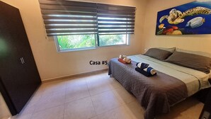 Een slaapkamer met een bed, een raam met zonwering, een schilderij aan de muur en een deur.