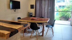 Een vergaderruimte met een houten tafel, zwarte stoelen, een flatscreen-tv, een koffieapparaat en een groot raam met gordijnen.