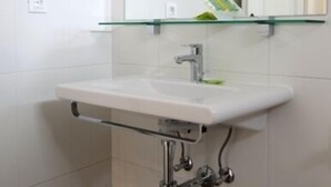 Une salle de bain avec un lavabo blanc, une étagère en verre au-dessus et un miroir.