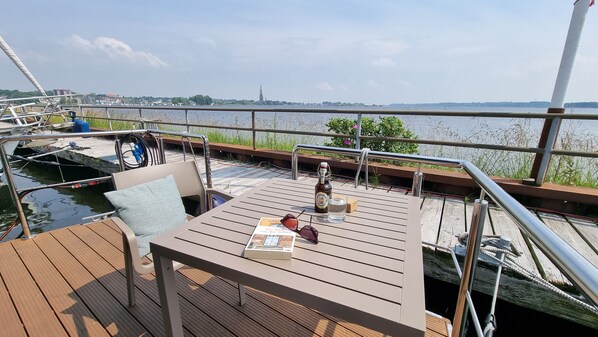 A wooden deck with a table, a bottle, and a glass. - Naturnaher Urlaub auf Hausboot Aava mit Dachterrasse in Schleswig (Schleswig)