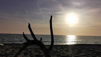 A beach with a large, weathered wooden structure in the foreground and the sun setting over the ocean.