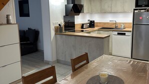 A modern kitchen with a wooden dining table, built-in appliances, and a view to a living area. - Comfortable house, seaside + Private Parking (Gruissan)