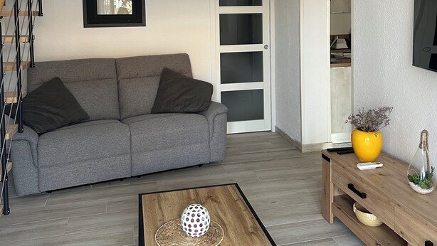 A modern living room with a grey sofa, a wooden coffee table, and a TV mounted on the wall. - Comfortable house, seaside + Private Parking (Gruissan)