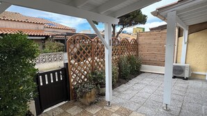 A covered patio with a tiled floor, a wooden fence, and a black gate. - Comfortable house, seaside + Private Parking (Gruissan)