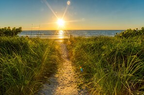 Rantapolkua, joka johtaa merelle, ja taustalla auringonlasku.