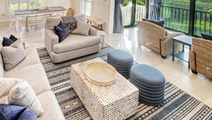 Ein geräumiges Wohnzimmer mit einer Couch, Poufs und einem Couchtisch, ein Essbereich mit Tisch und Stühlen sowie ein Balkon mit Meerblick.