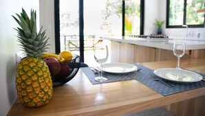 Une cuisine avec une table en bois mise pour deux personnes, agrémentée d’un ananas et d’un panier de fruits.