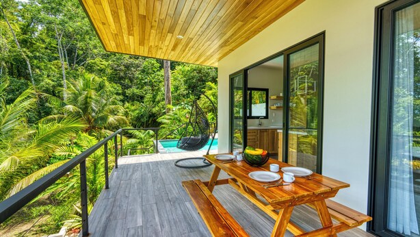 Une terrasse en bois avec une table dressée pour le repas, donnant sur un jardin luxuriant et une piscine.