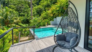 Un fauteuil suspendu au bord d’une piscine, avec vue sur une végétation luxuriante.