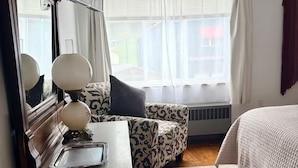 Un dormitorio con cama, cómoda, espejo, ventana con cortinas y radiador.