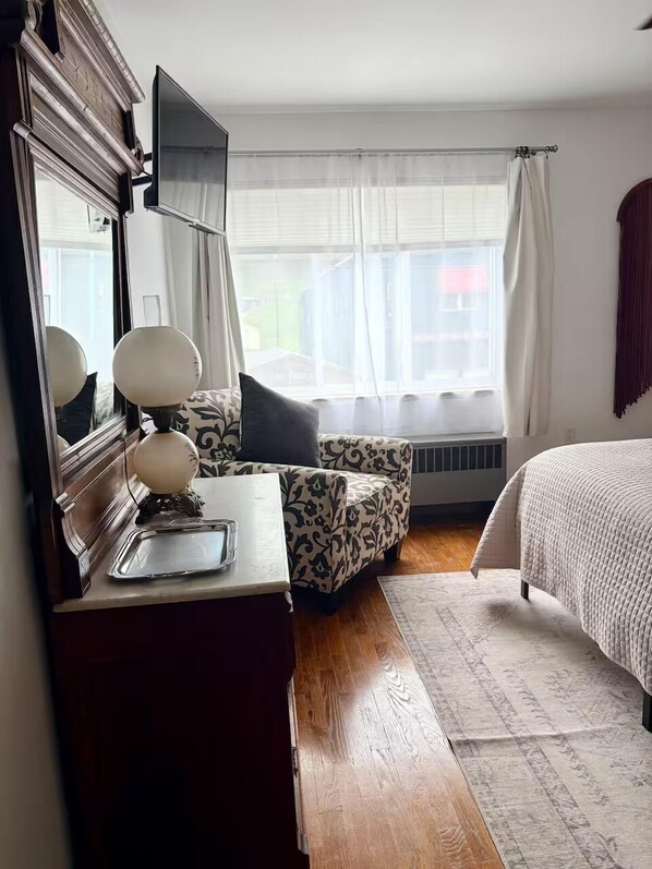 Une chambre à coucher avec un lit, une commode, un miroir, une fenêtre avec des rideaux et un radiateur.