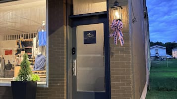 A storefront with a dark brick facade, a clear glass window displaying clothing, a small potted plant, and a door with a sign.