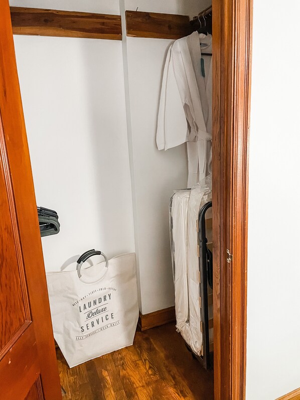 Une buanderie avec un plancher en bois, un mur blanc et un étendoir. On aperçoit un sac blanc avec du texte posé sur le sol.
