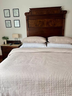 A bed with a quilted cover, a wooden headboard, and a bedside table with a lamp and a clock.