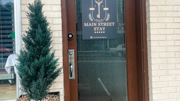 Una puerta marrón con un letrero que dice 'Main Street Stay' y una dirección web.