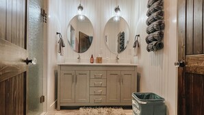 A bathroom with wooden walls, a stone-tiled floor, a large mirror, and a green trash bin.