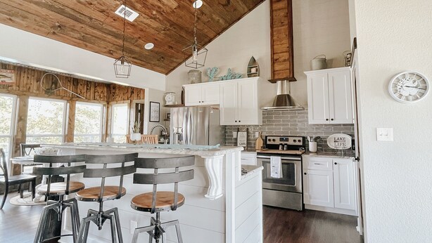 A spacious kitchen with wooden ceiling beams, white cabinetry, and a central island with stools.