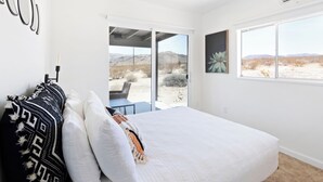 Een slaapkamer met een groot bed, een plafondventilator en uitzicht op een woestijnlandschap door het raam.