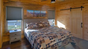 Une chambre à coucher dans un chalet en bois, avec un lit, des tables de chevet et une fenêtre donnant sur les montagnes.