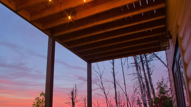 Un espace avec un bain à remous, doté d’un plafond en bois et offrant une vue sur les arbres se découpant sur un coucher de soleil.