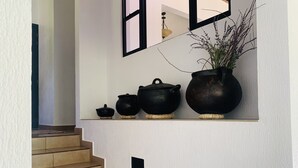 A staircase with beige tiles leading to a landing where three black pots are displayed on a shelf, accompanied by a potted plant with purple flowers. - Casa completa dentro de un complejo privado con seguridad 24/7 (La Libertad)
