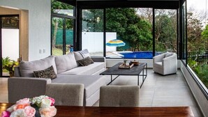 A modern living room with a sofa, armchairs, a coffee table, and a view of a swimming pool and greenery outside. - Casa completa dentro de un complejo privado con seguridad 24/7 (La Libertad)